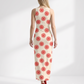 A chic sleeveless bodycon maxi dress featuring a soft ivory base with vibrant red floral sunburst prints, offering a fresh, elegant, and timeless look.