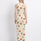 An elegant sleeveless bodycon maxi dress featuring a soft ivory base with scattered autumn leaf prints in earthy green, beige, and rust tones, creating a fresh, nature-inspired look.