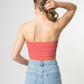 A minimalist strapless tube top in a soft coral pink with a smooth, clean, and vibrant finish.